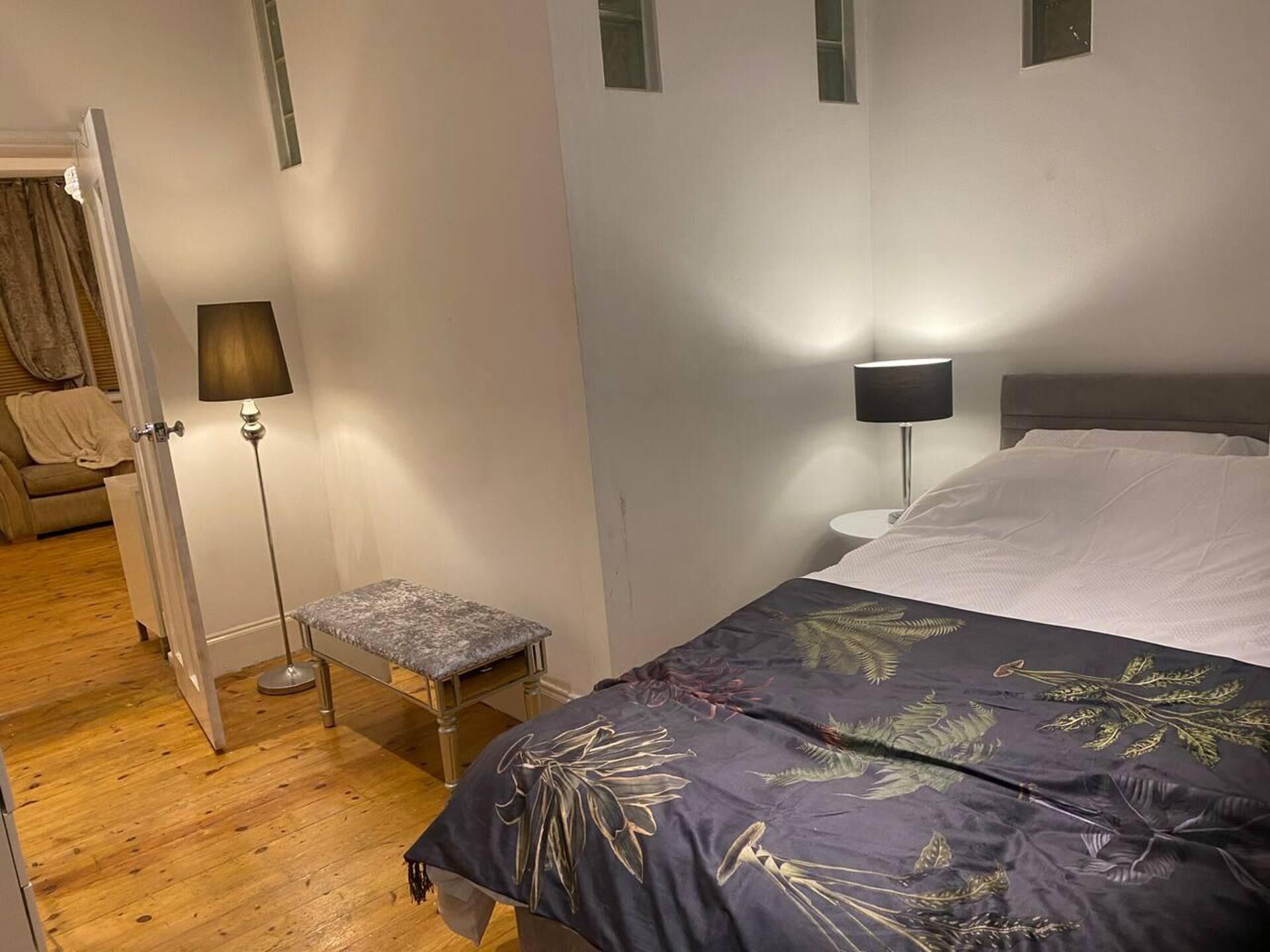 A bedroom with a bed, a nightstand, a lamp, a bench, and a door.