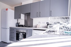A modern kitchen with grey cabinets, a white refrigerator, a built-in oven, and a dishwasher. - 2-bed House With Canal View, Garden & Petsok (Salford)
