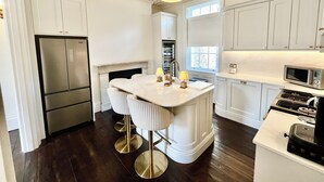 Une cuisine moderne avec des meubles blancs, un îlot central doté de tabourets de bar, un réfrigérateur en acier inoxydable, un four à micro-ondes et une cuisinière à gaz.