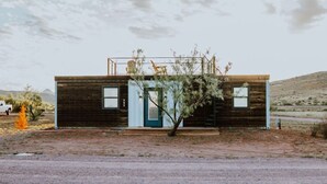 Eine moderne Blockhütte mit blauer Tür, einer kleinen Veranda und einem Baum davor.