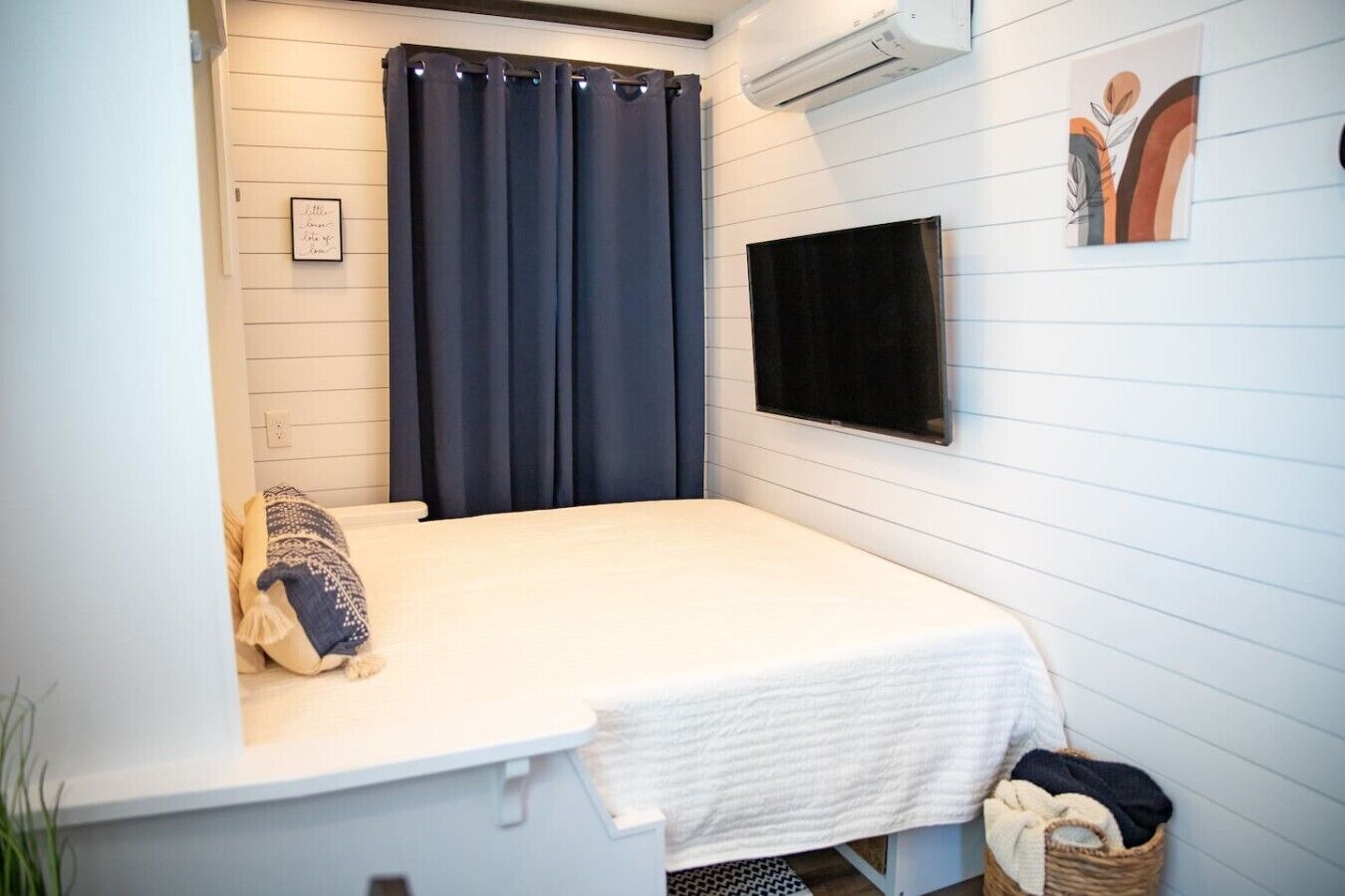 Una piccola camera con un letto singolo, tenda scura, TV a muro e condizionatore d'aria.