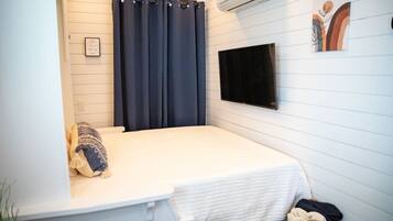 Una piccola camera con un letto singolo, tenda scura, TV a muro e condizionatore d'aria.