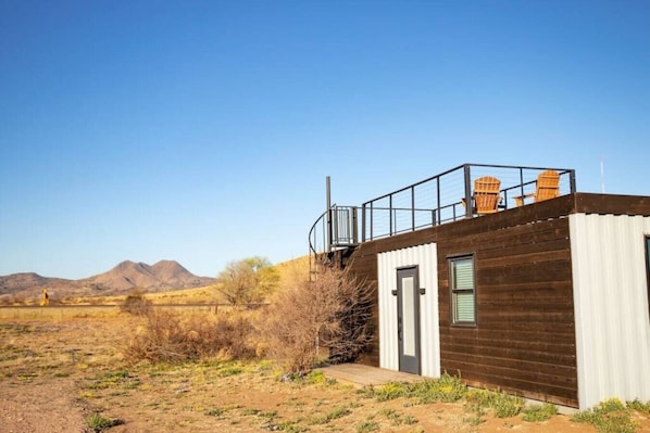 Ein kleines Gebäude mit Holzfassade, einer Metalltreppe und einem Balkon mit Stühlen.