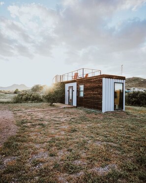 A modern cabin with a wooden exterior, a balcony with a chair, and a door leading to the interior. - New! Endless Sunsets-Container Home (Alpine)