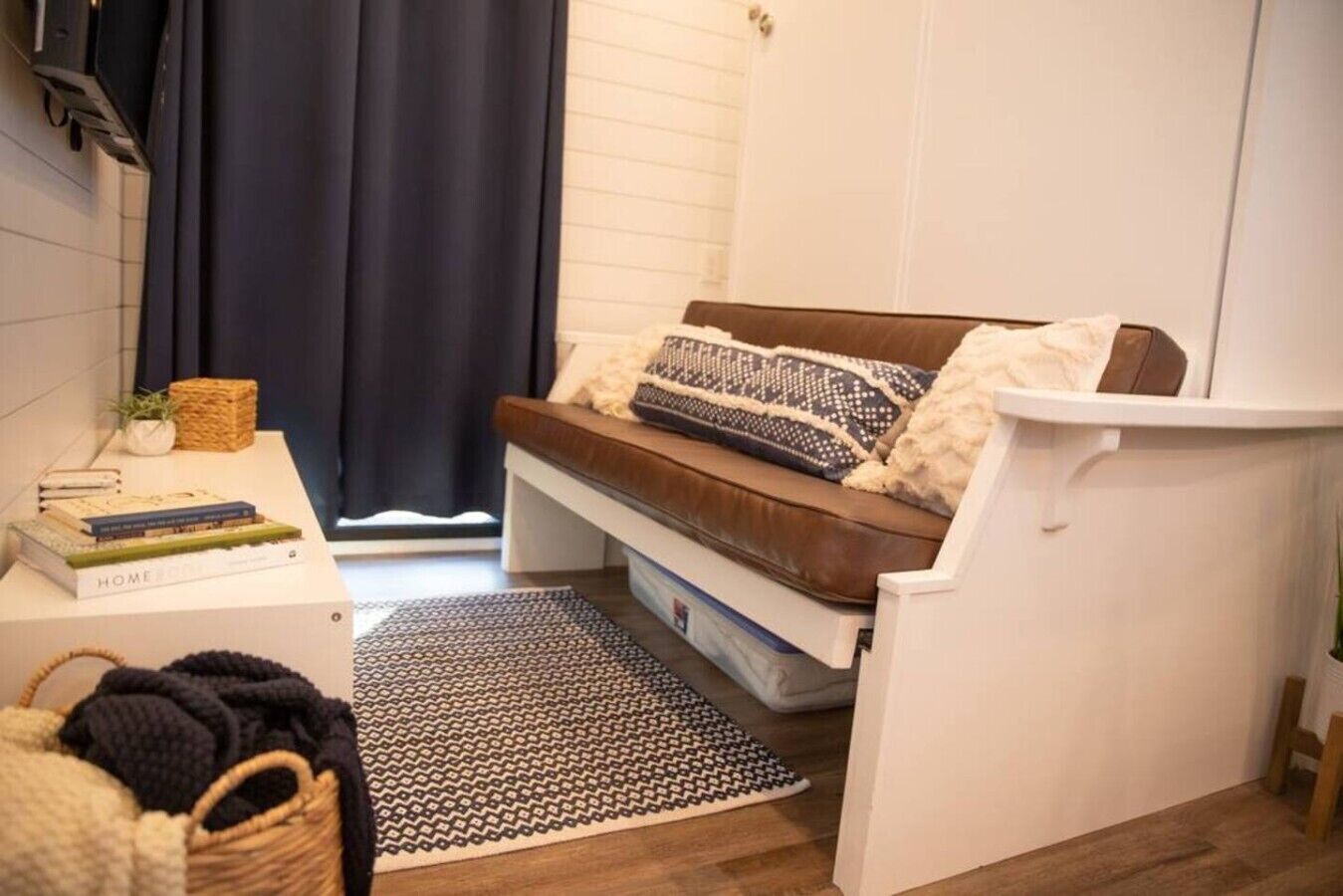 Een gezellig, klein leefruimte met een bank, een tafeltje met boeken, een mand en een raam met gordijnen.