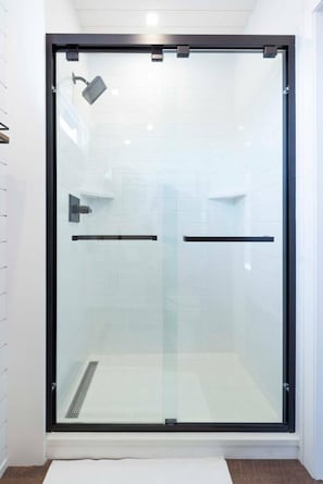 A glass-enclosed shower with a black frame, a white tiled wall, and a white floor.
