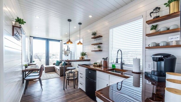 A modern kitchen with a central island, pendant lighting, and built-in shelving. - The Stardust Stunning Container Home (Alpine)