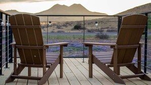 Two wooden Adirondack chairs on a wooden deck with a view of a mountain and purple flowers. - The Stardust Stunning Container Home (Alpine)