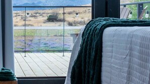 A bedroom with a large window, a bed, and a view of mountains. - The Stardust Stunning Container Home (Alpine)