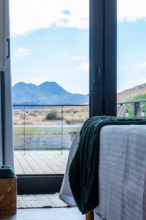 A bedroom with a large window, a bed, and a view of mountains.