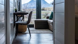 A room with a view of mountains, a table with a chair, and a sofa with a cushion. - The Stardust Stunning Container Home (Alpine)