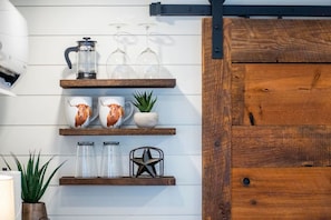 A kitchen with wooden shelves holding mugs, a coffee maker, glasses, and a star-shaped container.