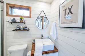 Ein Badezimmer mit Toilette, Waschbecken, Holzregalen, einem Spiegel und einem Bilderrahmen mit der texanischen Flagge.