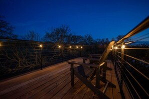 Eine Holzterrasse mit Stühlen und Lichterketten, umgeben von einem Metallgeländer.