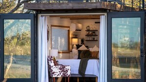 A cozy interior with a bed, a chair, and a table, and a large window offering a view of the outdoors. - The Lone Star Shipping Container | Rooftop Patio (Fredericksburg)