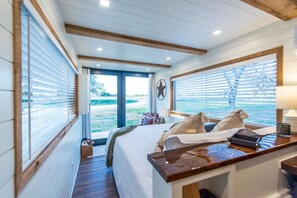 A bedroom with a bed, bedside table, and a window with a view of the outdoors. - The Lone Star Shipping Container | Rooftop Patio (Fredericksburg)