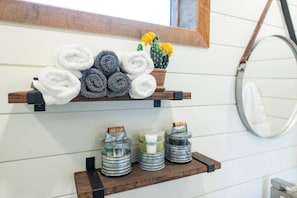 Un baño con estantes de madera que sostienen toallas enrolladas y artículos de tocador.