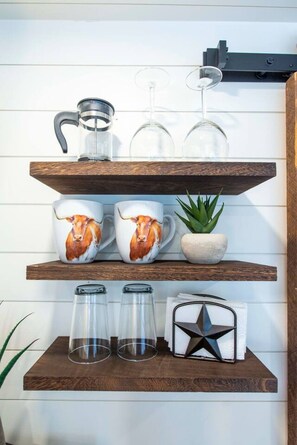 A wooden shelf with kitchenware, a potted plant, and a star-shaped object. - The Lone Star Shipping Container | Rooftop Patio (Fredericksburg)