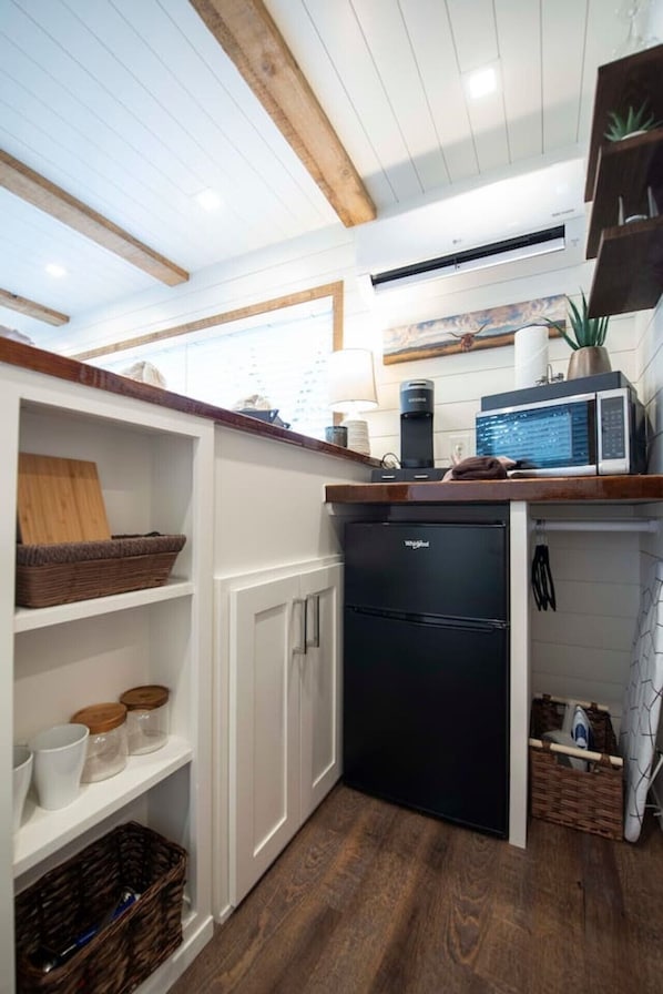 Eine kompakte Küche mit weißen Schränken, einem schwarzen Kühlschrank und einer Holz Arbeitsplatte.