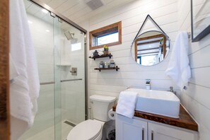 Ein modernes Badezimmer mit Duschkabine aus Glas, Toilette, Waschbecken mit Holztischplatte und Spiegel über dem Waschbecken.