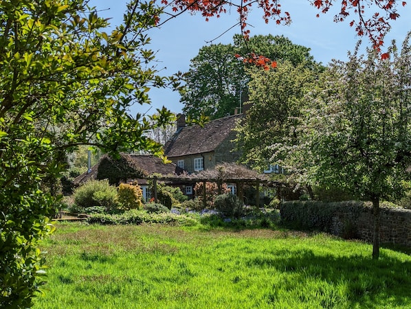Una casa in pietra tradizionale con tetto in tegole, immersa nel verde e circondata da piante fiorite.