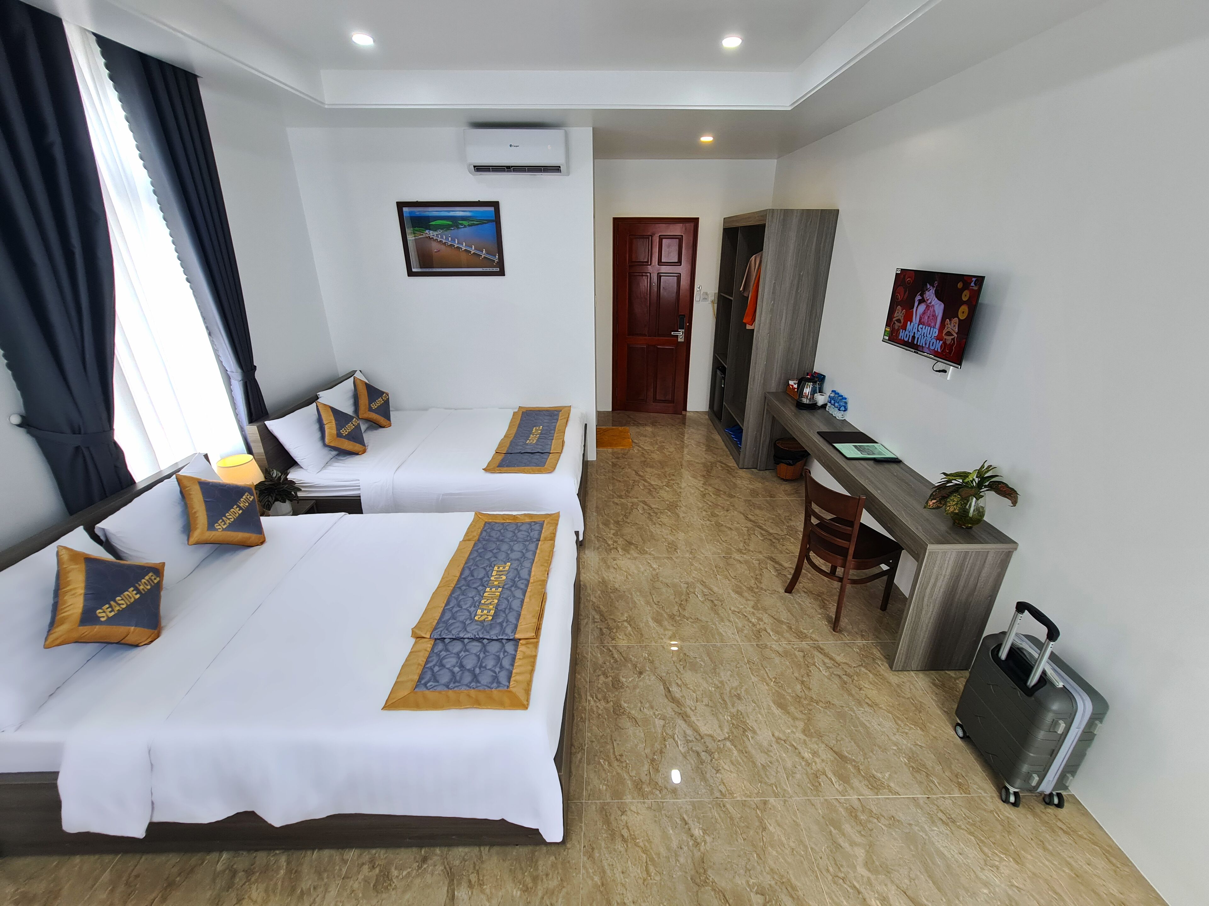 Habitación de hotel con dos camas, un escritorio, una silla, un televisor y una maleta.
