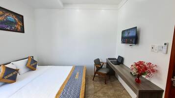 A hotel room with a bed, a desk, a chair, a television, and a vase with flowers.