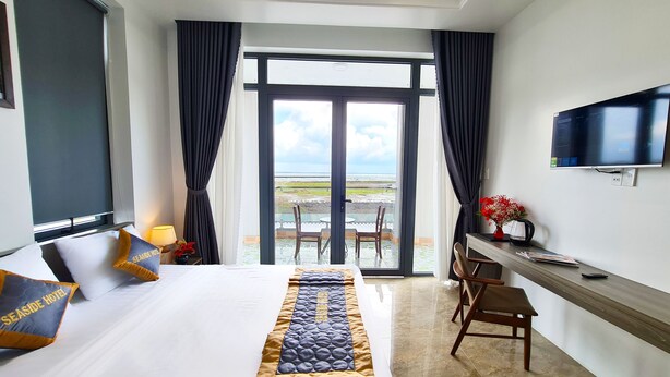 A hotel room with a bed, a desk, a TV, and a view of the sea. - Seaside Hotel (Rach Gia)