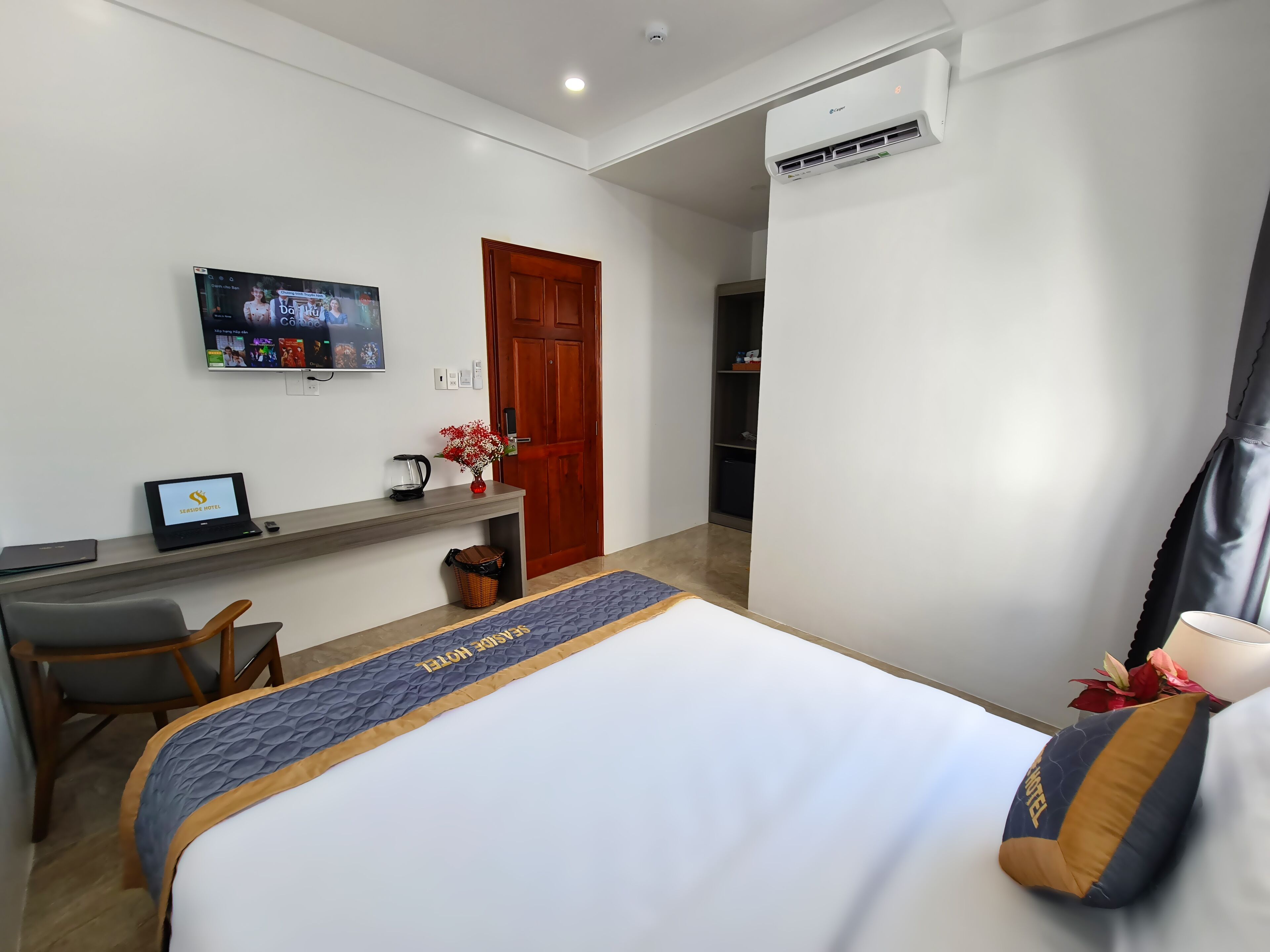 Habitación de hotel con cama, escritorio, laptop, televisor y armario.