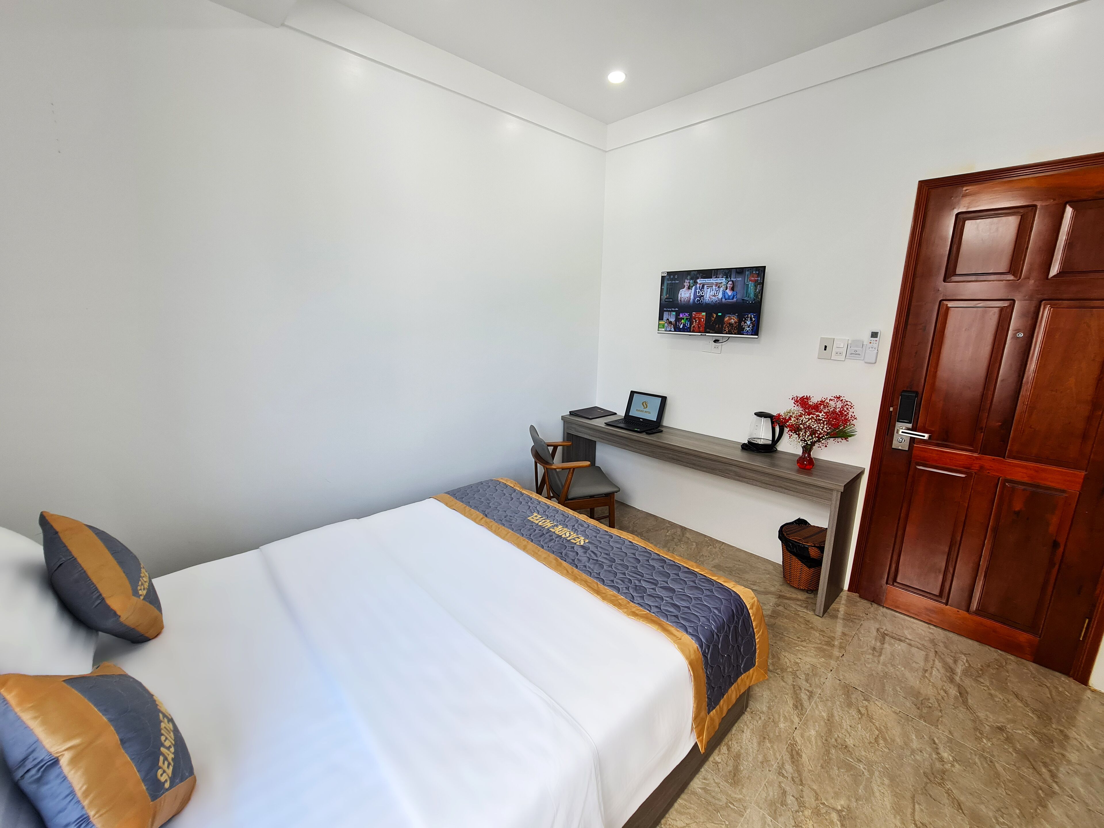 A hotel room with a bed, a desk with a laptop, a television, and a wooden door.