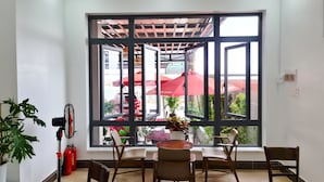 A room with a large window, a table with chairs, a potted plant, and a fire extinguisher. - Seaside Hotel (Rach Gia)