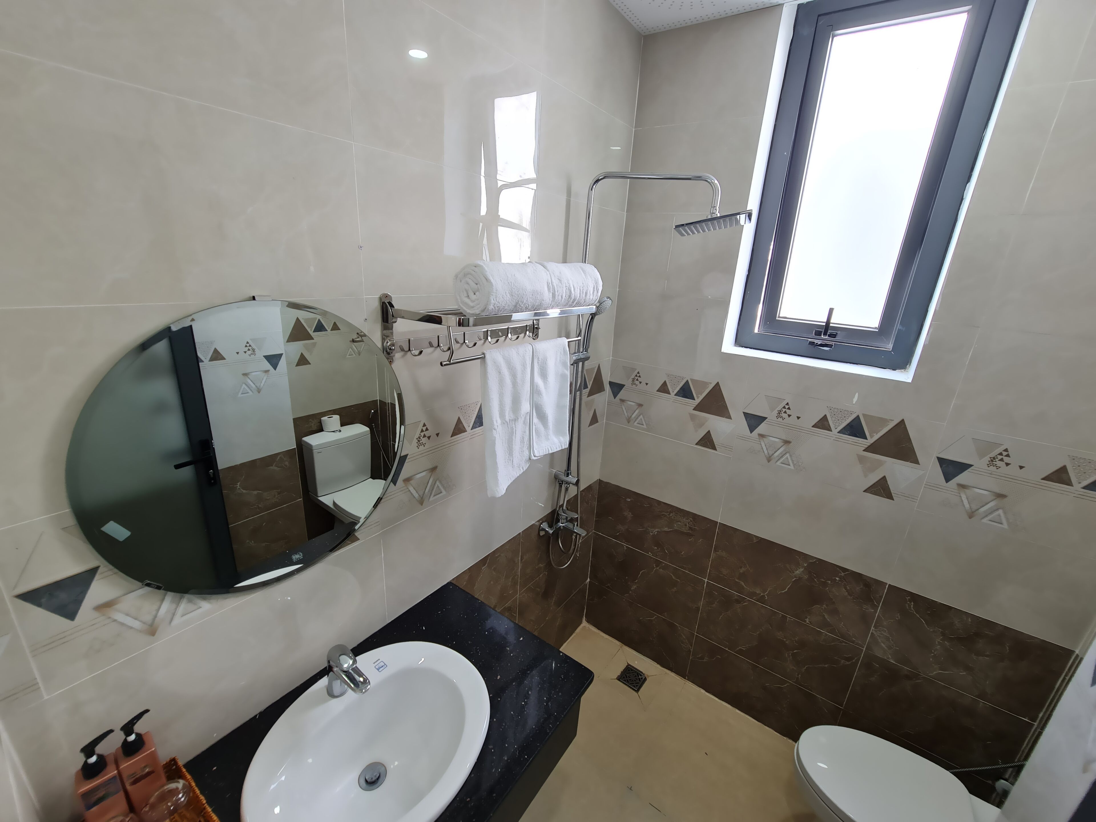 Un baño moderno con un espejo redondo, dos lavamanos, un inodoro y una ducha.