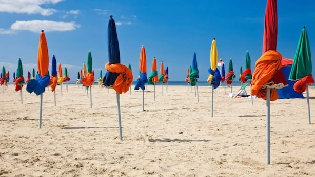 Una playa con hileras de sombrillas y sillas de colores.