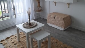 Una sala moderna con un mueble de televisión blanco, un pouf tejido, una mesita con un florero y una alfombra grande tejida.