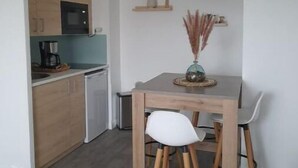 Una cocina compacta con microondas, cafetera y lavavajillas. Hay una mesa de comedor con dos sillas y una lámpara colgante sobre ella.