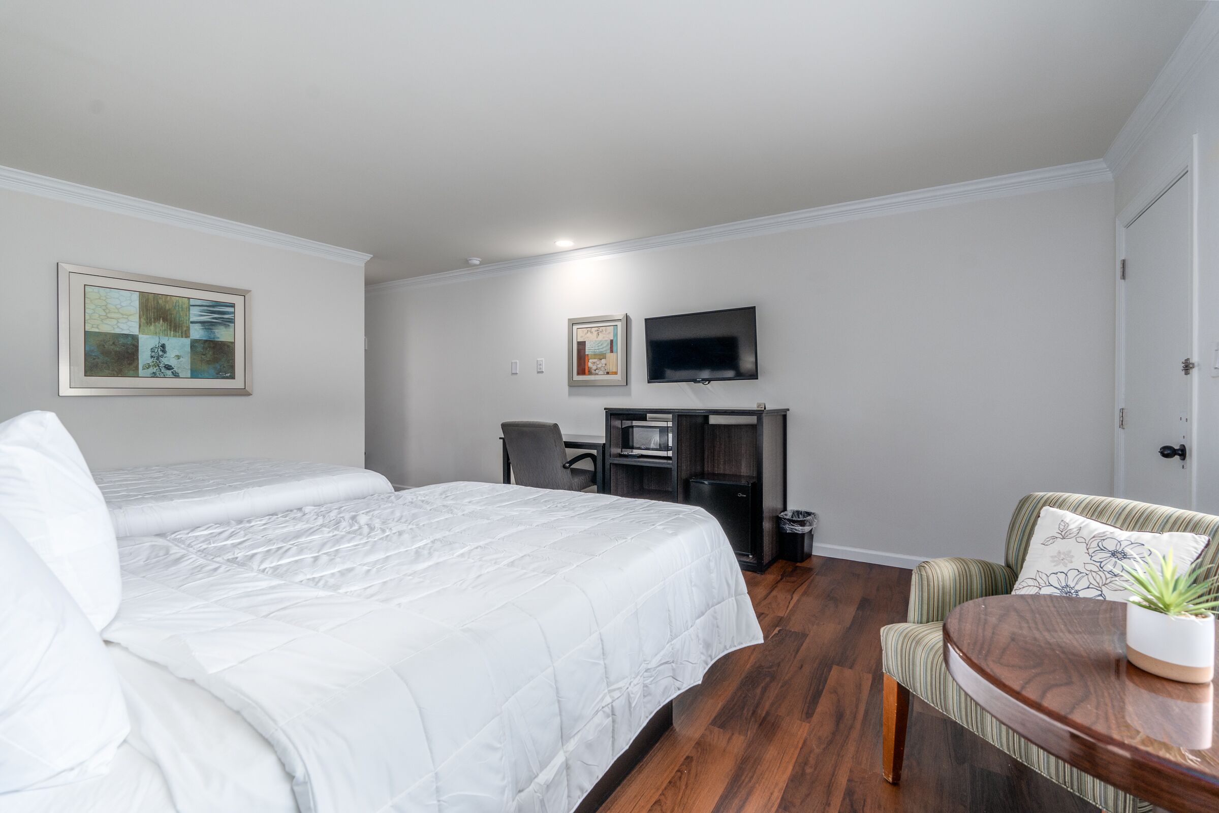 A hotel room with two beds, a desk, a television, and a chair.