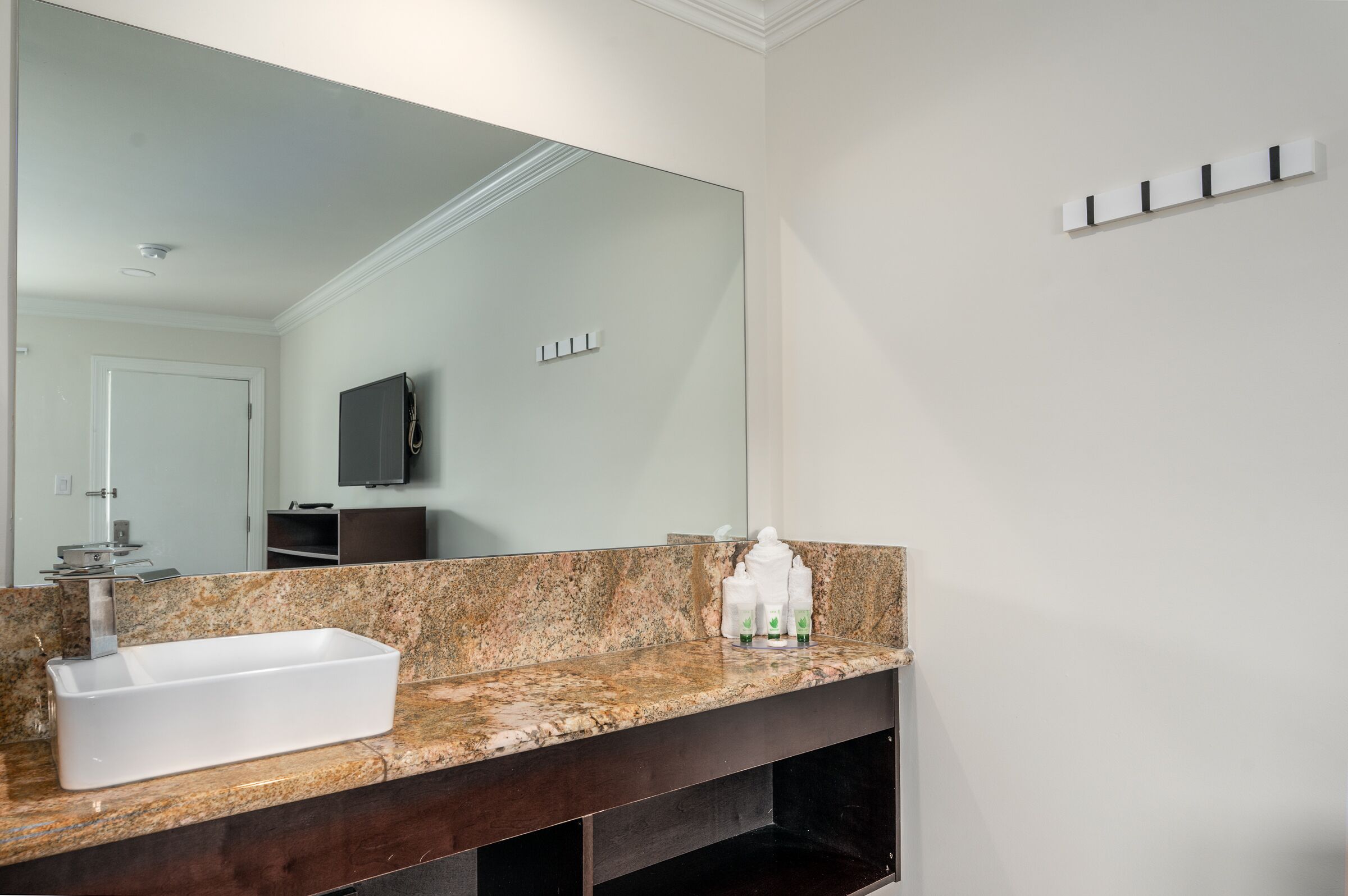 Ein Badezimmer mit einer Granitplatte, einem rechteckigen Waschbecken, einem großen Spiegel und einem Handtuchhalter an der Wand.