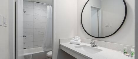 Ein Badezimmer mit einer weißen Marmordusche, einem weißen Waschbecken inklusive Spiegel und einer weißen Toilette.