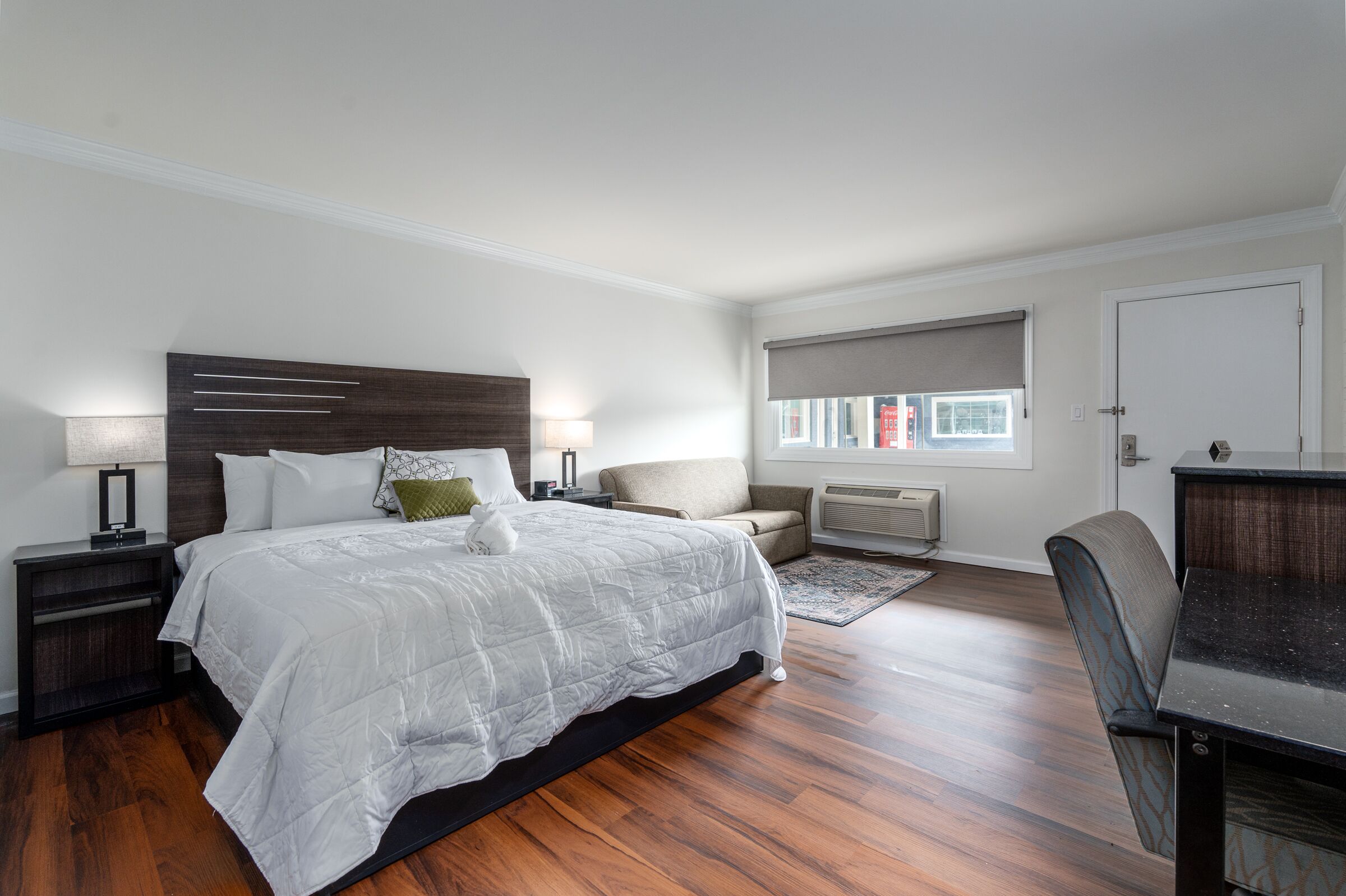 A bedroom with a large bed, bedside tables, a chair, a desk, and a window with blinds.
