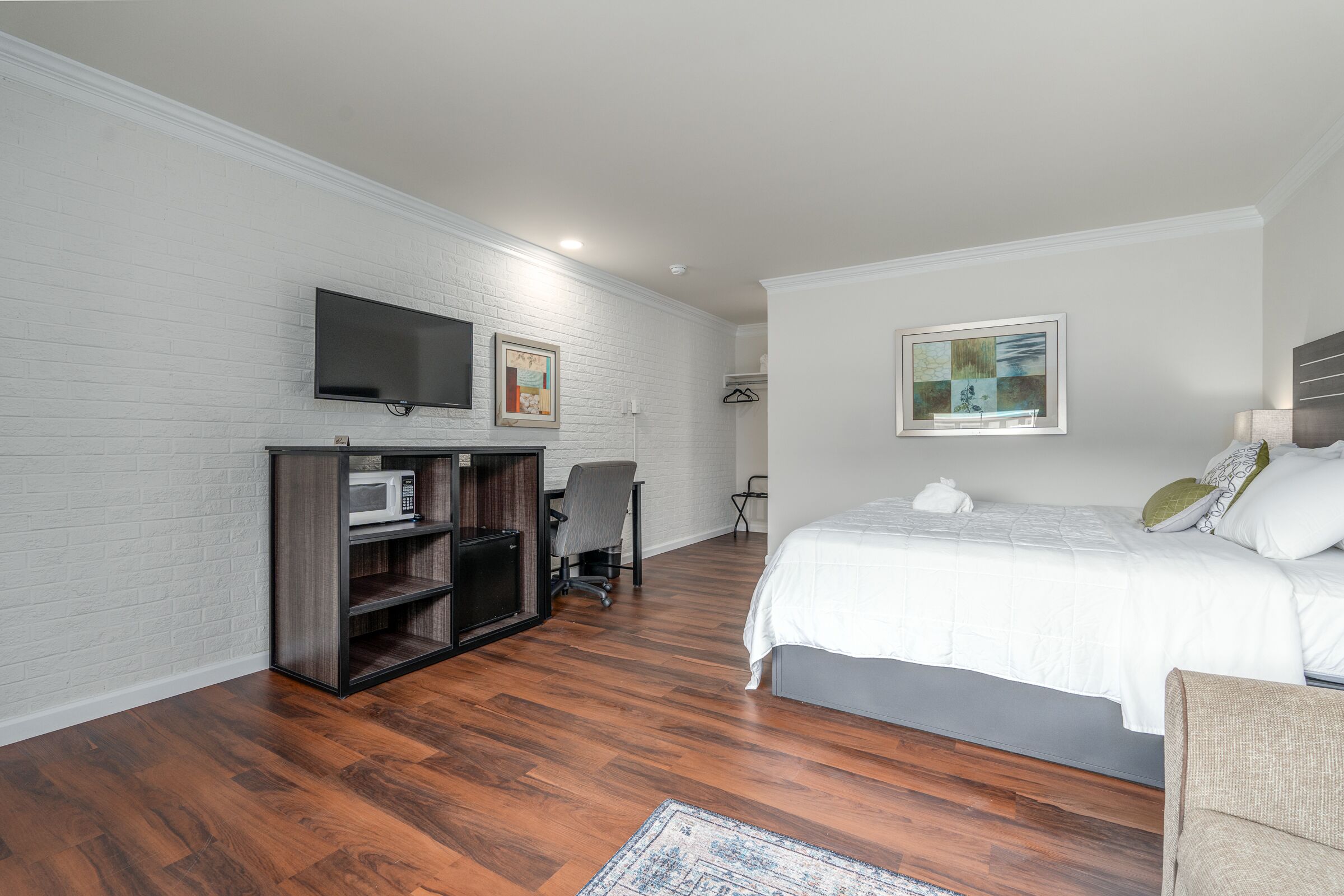 A bedroom with a bed, a TV mounted on the wall, a desk with a chair, and a small seating area.