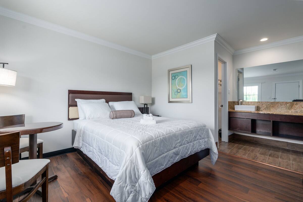 Ein Hotelzimmer mit Bett, Nachttisch, Stuhl und einem Badezimmer mit Waschbecken und Spiegel.