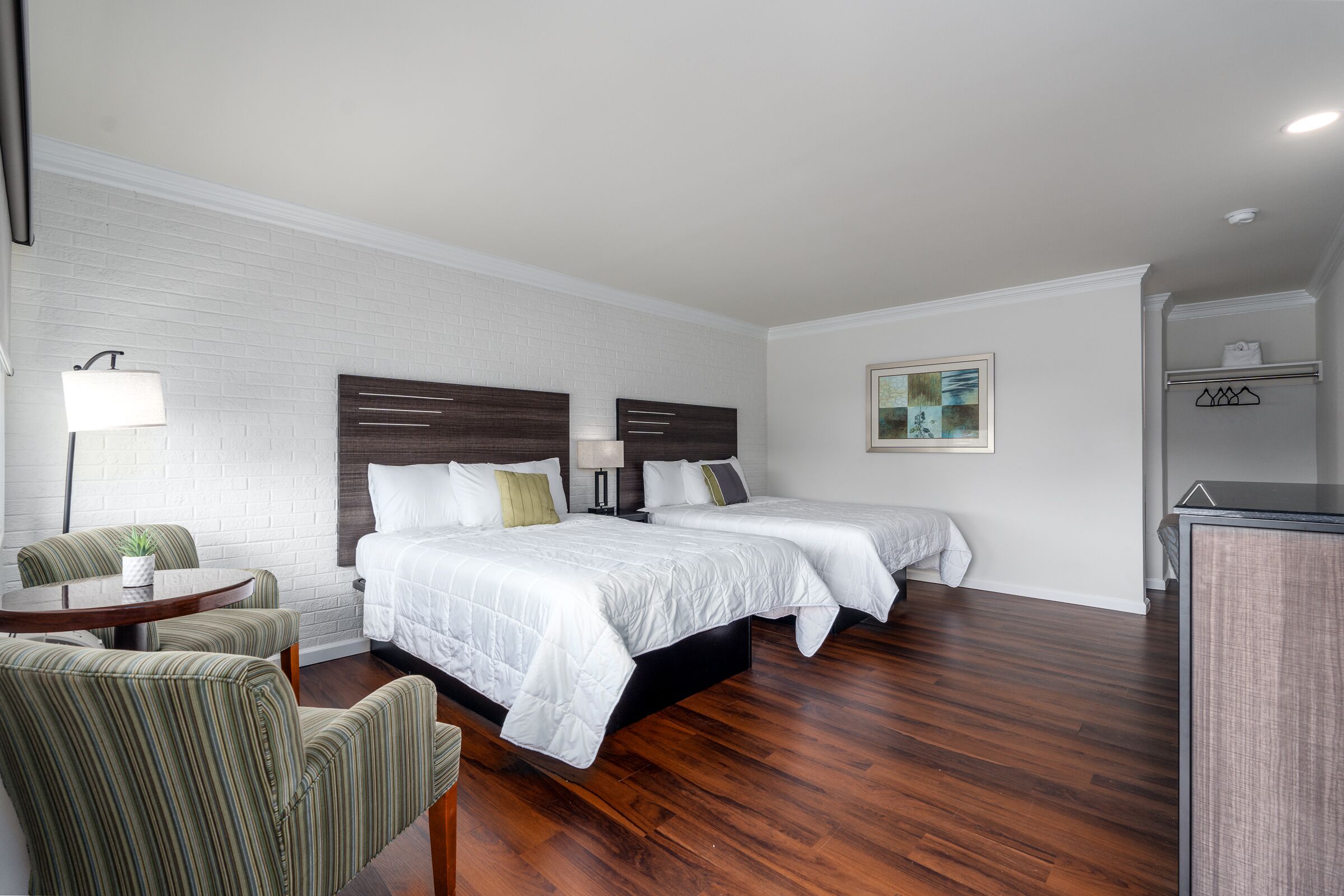 Habitación de hotel con dos camas, un escritorio, una silla, una lámpara y un cuadro en la pared.