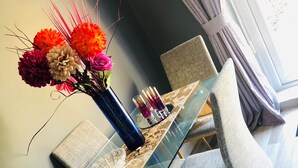 Un comedor moderno con una mesa de vidrio, sillas tapizadas grises y un jarrón de flores.