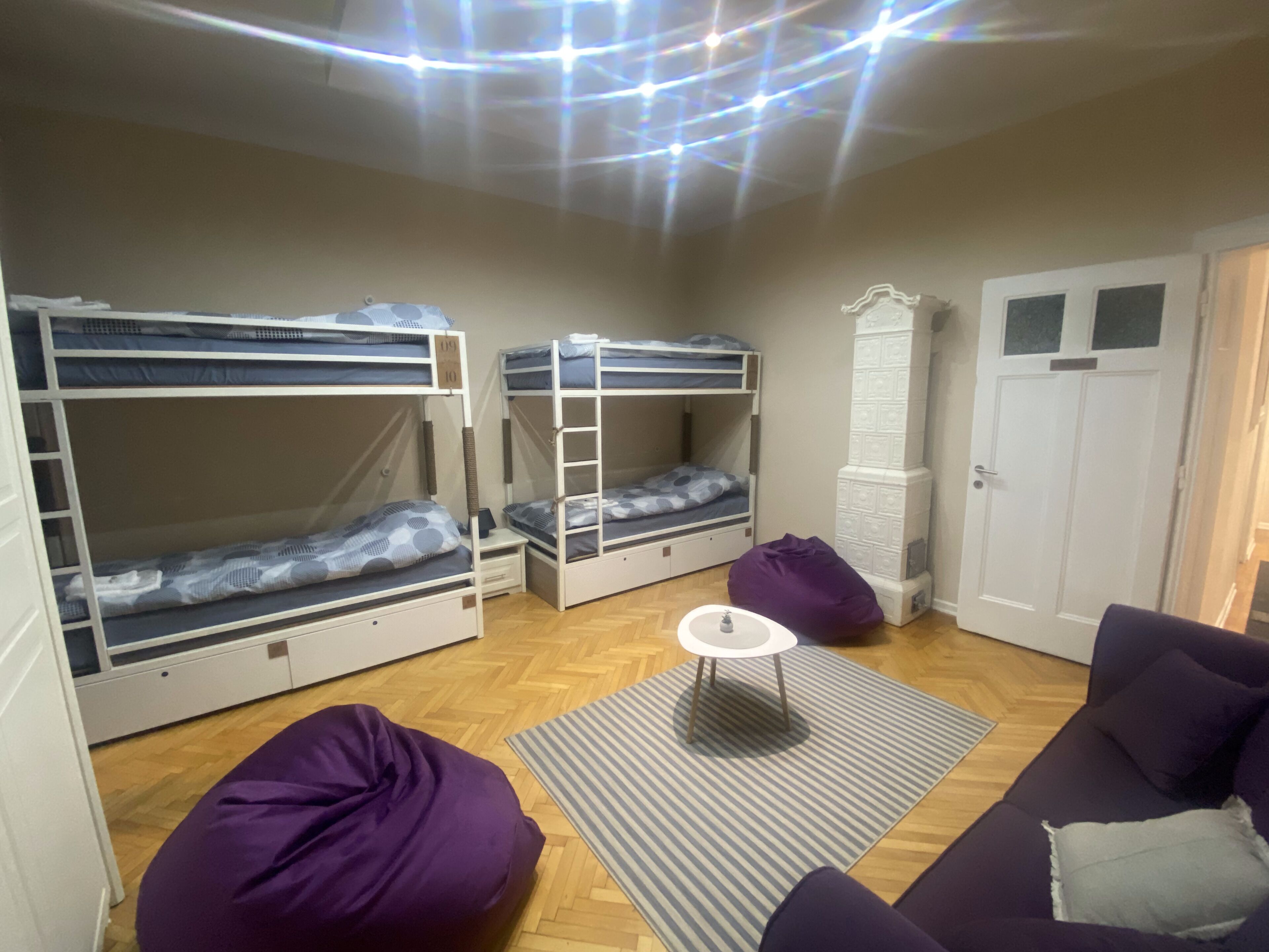 Una habitación con literas, un sillón de peluche morado, una mesita blanca pequeña y una alfombra estampada.