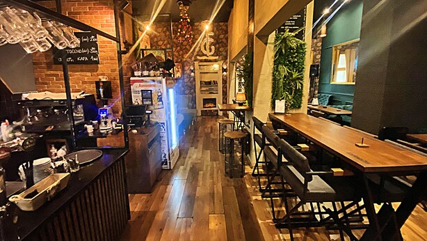 A cozy bar area with wooden flooring, bar stools, and a counter displaying various items. - FG Boutique Hostel (Sarajevo)