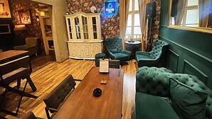 A cozy room with a wooden dining table, green upholstered sofas, a white cabinet, and floral wallpaper. - FG Boutique Hostel (Sarajevo)