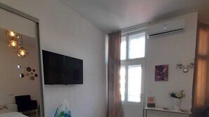 A modern bedroom with a bed, a TV, a small desk, a window with curtains, and a patterned rug. - FG Boutique Hostel (Sarajevo)