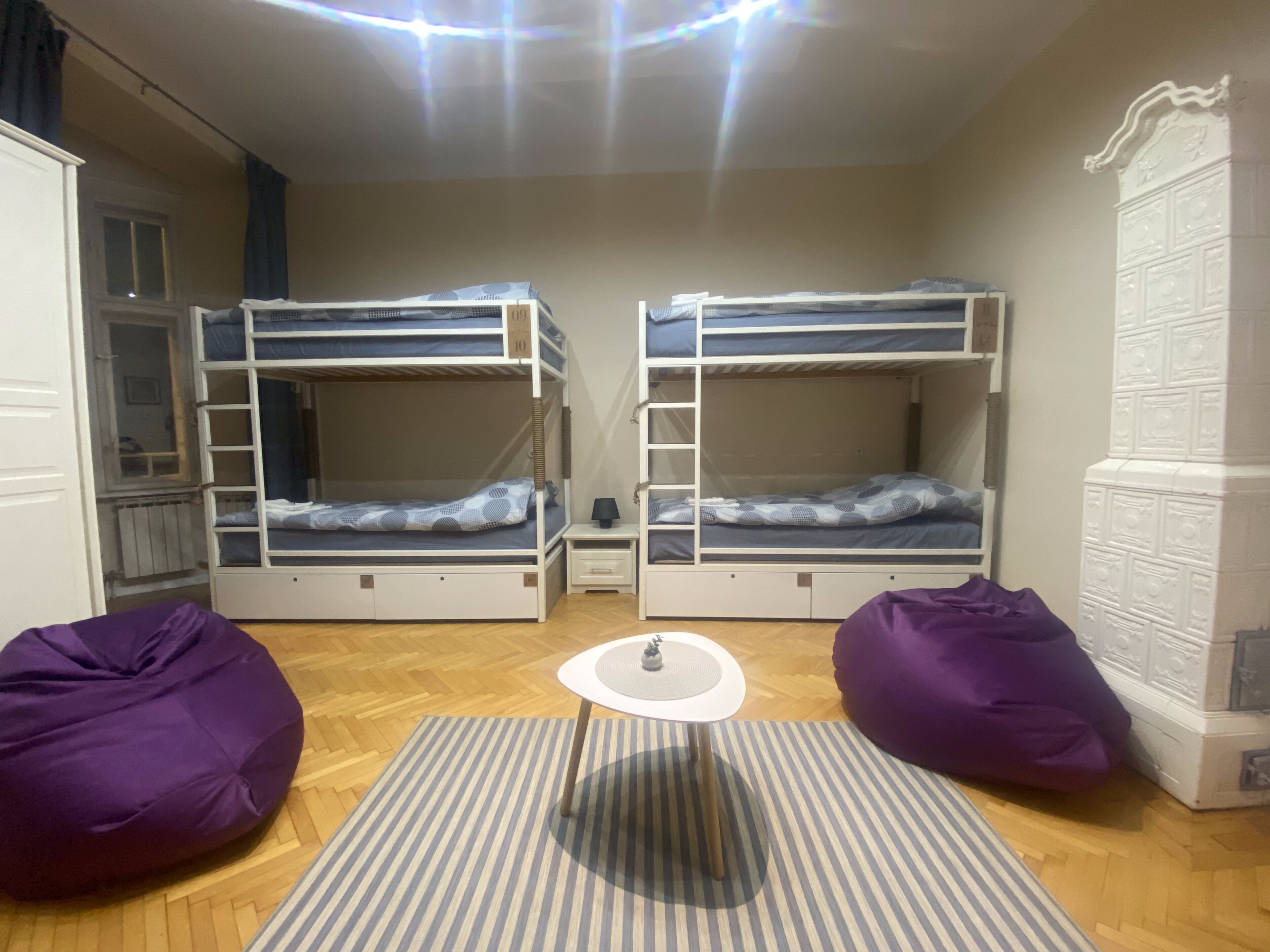 A room with two bunk beds, a small table, two bean bags, and a radiator.