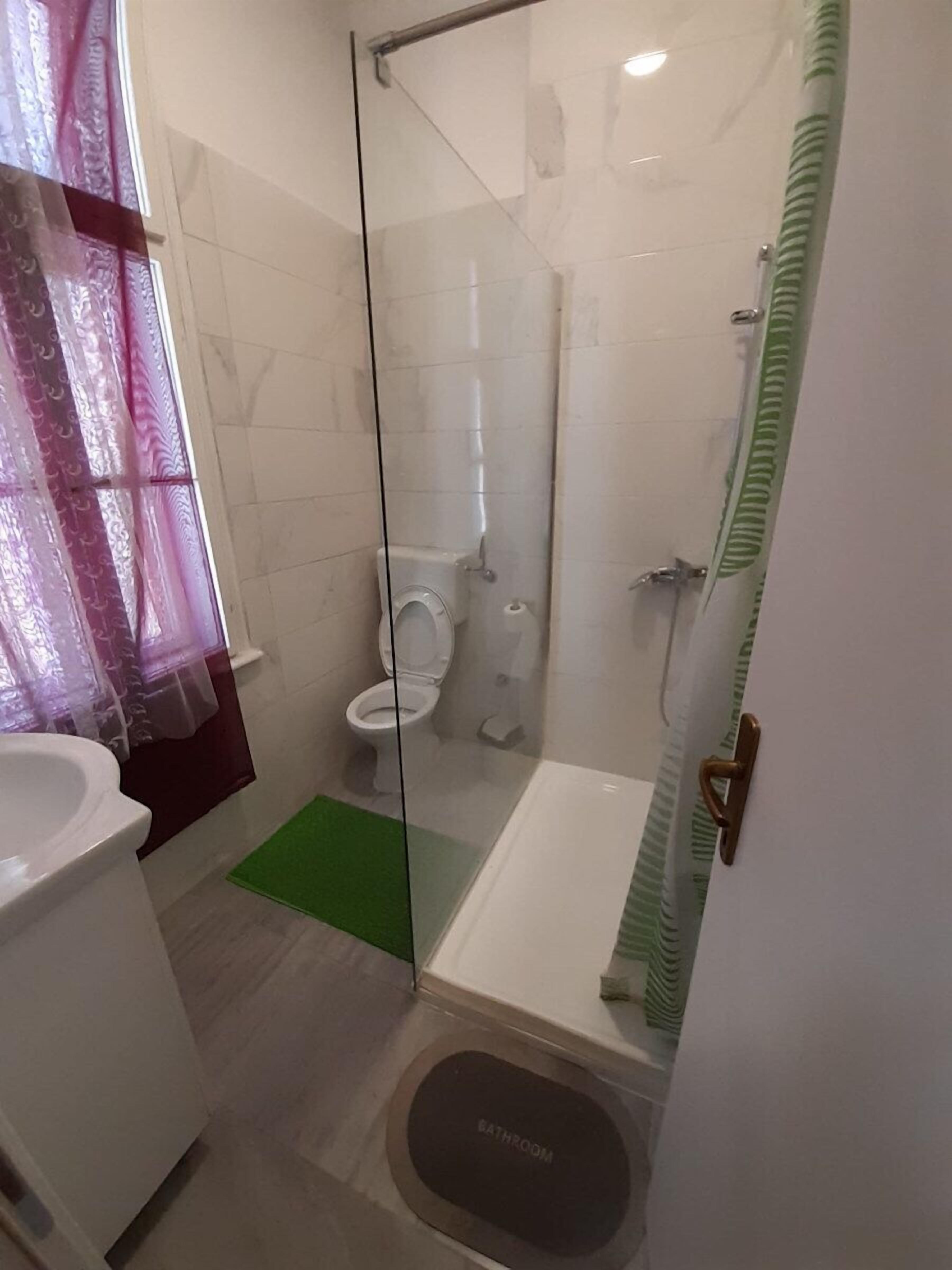 A bathroom with a glass partition, a toilet, a shower, and a sink.