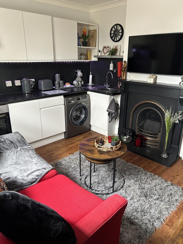 A modern kitchen with a washing machine, a dining area with a red sofa, and a fireplace.